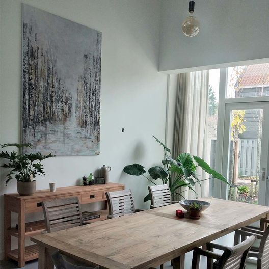 grijs blauw schilderij op lichtgroene muur boven houten eettafel