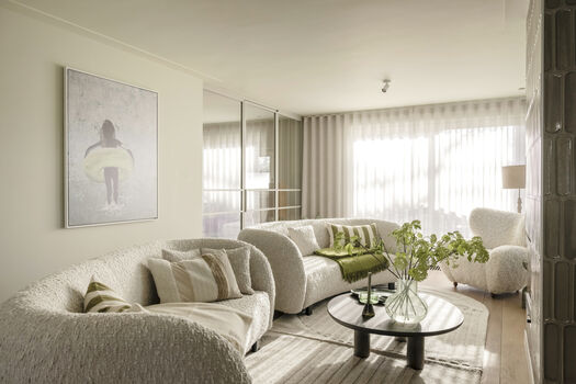 Lichte woonkamer met beige banken, groene accenten, ronde salontafel en groot kunstwerk