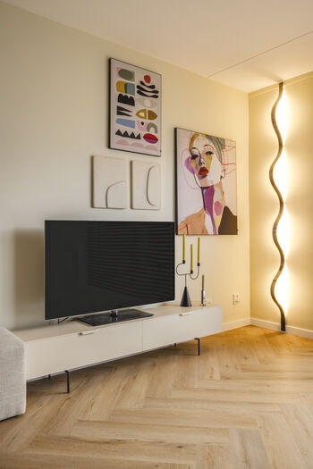 Moderne woonkamer met wit tv-meubel, kleurrijke wandkunst en golvende vloerlamp op houten vloer
