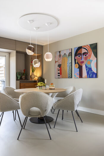 Moderne eethoek met ronde tafel, beige stoelen, hanglampen en kleurrijke wandkunst