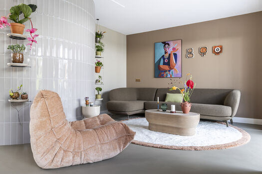 Kleurrijke woonkamer met roze lounge stoel, grijze bank, plantenwand en moderne kunst