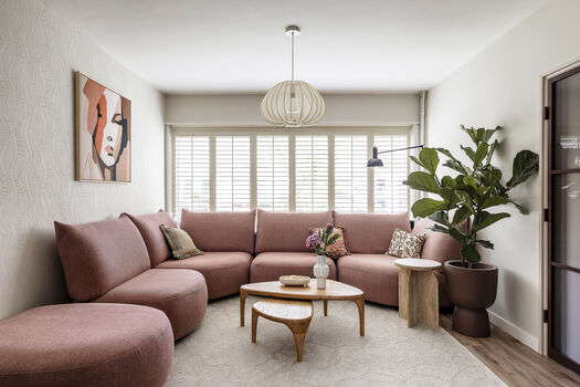 Woonkamer met roze hoekbank, houten salontafel, grote plant en abstract portret aan de muur