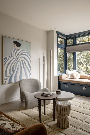 Rustige woonkamer met beige fauteuils, vensterbank, kaarsen en abstract portret