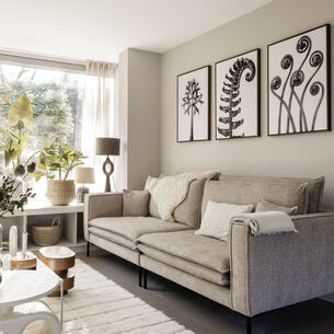 Sfeervolle woonkamer met beige bank, houten accenten en botanische kunst in zwart-wit