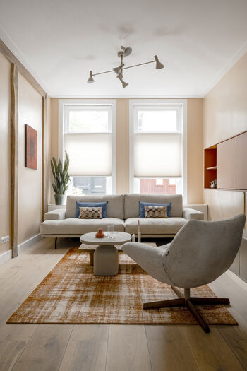 Minimalistische Japandi woonkamer met beige bank, oranje vloerkleed en abstract kunstwerk