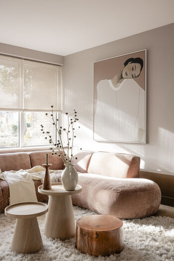 Warme woonkamer met roze bank, houten bijzettafels, wit vloerkleed en portret van vrouw