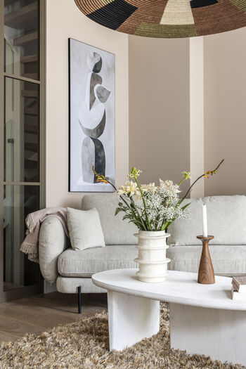 Serene woonkamer met beige bank, witte ronde salontafel, abstract kunstwerk met geometrische vormen