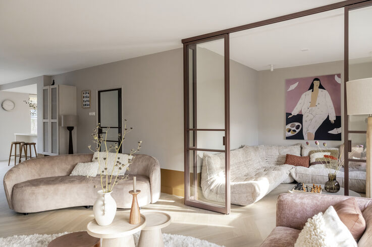 Lichte woonkamer met gebogen roze bank, glazen schuifwand en een kunstwerk van een vrouw in witte kleding