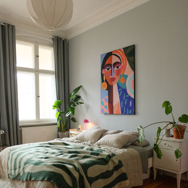 Slaapkamer met groot kleurrijk schilderij boven bed, groene planten en grijs-groene accenten.