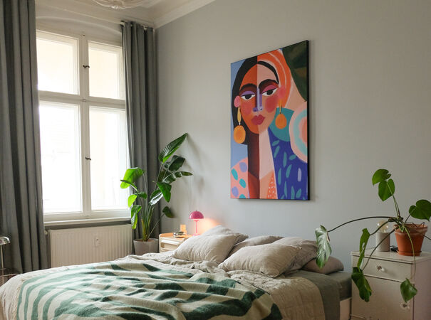 Slaapkamer met groot kleurrijk schilderij boven bed, groene planten en grijs-groene accenten.