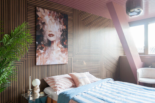 Slaapkamer met houten wandpanelen, modern kunstwerk boven bed en roze-blauwe accenten.