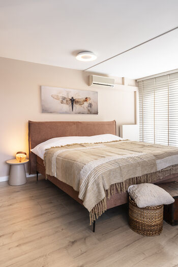 Slaapkamer met beige tinten, groot bed met sprei, wandkunst met insect en houten vloer
