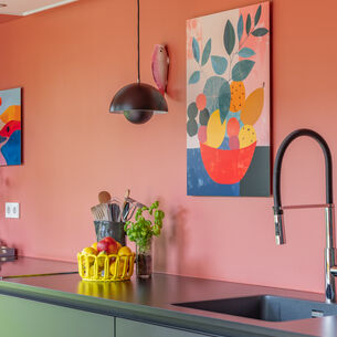 Keuken met roze muur, kleurrijke kunstwerken en modern kookeiland met fruit en bloemen