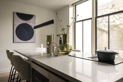 Strakke keuken met groot raam, wit kookeiland en abstract kunstwerk met cirkels