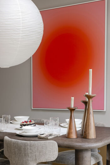 Eetkamer met grote rode wandkunst, houten tafel en moderne kandelaars