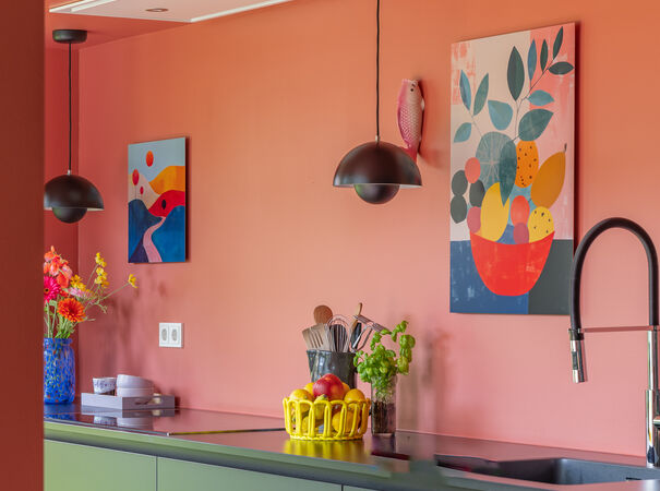 Keuken met roze muur, kleurrijke kunstwerken en modern kookeiland met fruit en bloemen