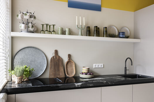 Moderne keuken met zwart werkblad, houten snijplanken en open plank vol servies en glazen