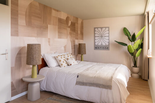 Slaapkamer met houten accentmuur, wit beddengoed, Matisse poster en grote groene plant