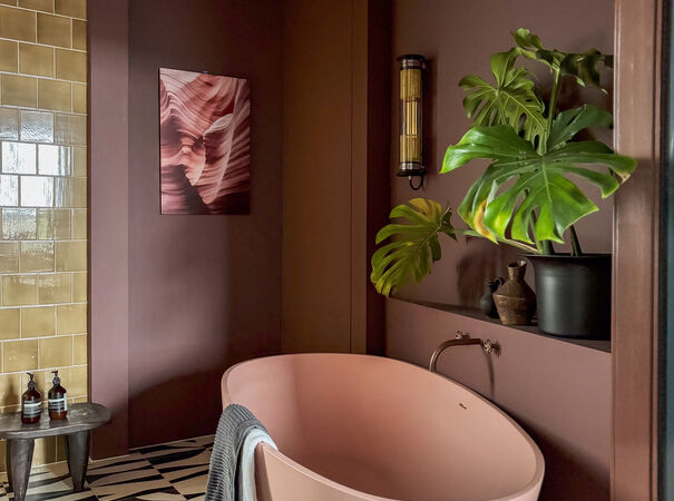 Luxe badkamer met roze bad, bruine muren, groene plant en kunstwerk