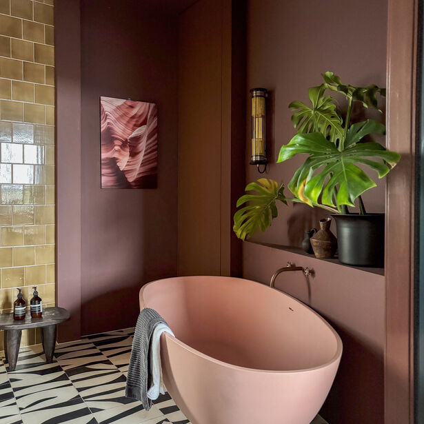 Luxe badkamer met roze bad, bruine muren, groene plant en kunstwerk