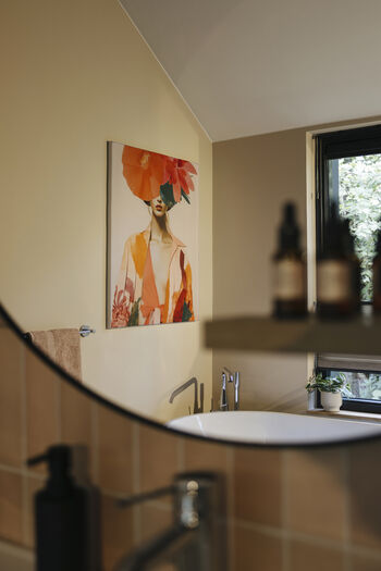Moderne badkamer met vrijstaand bad, kleurrijk vrouwenportret aan muur en houten accenten.
