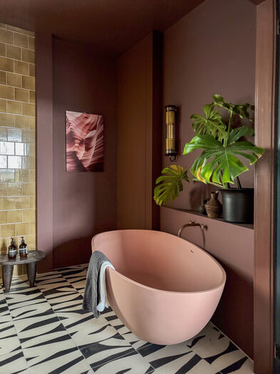 Roze badkamer met roze vrijstaand bad, geometrische vloer, groene plant en abstracte kunst