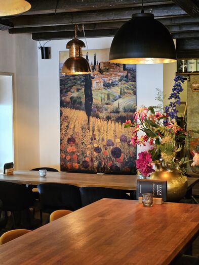 Kantoor restaurant met houten tafels, bloemen en kleurrijke muurschildering.