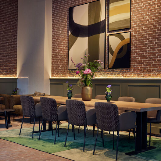 Moderne vergaderruimte met grote houten tafel, designstoelen en abstracte kunst.