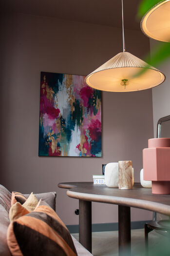 Abstract kleurrijk schilderij aan grijze muur boven eettafel met roze accessoires