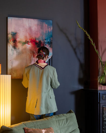 Vrouw in groen jasje bij abstract kleurrijk kunstwerk aan donkere muur