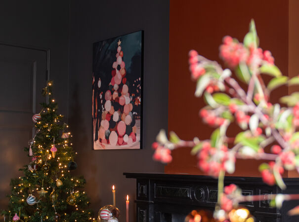 Kerstsfeer met verlichte boom en kleurrijk schilderij boven zwarte schouw