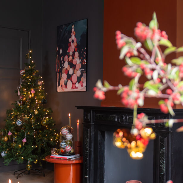 Kerstsfeer met verlichte boom en kleurrijk schilderij boven zwarte schouw