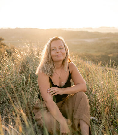 Photo of artist Raisa sitting in sand dunes