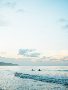 Photo of surfers in a blue sea, under the blue sky.