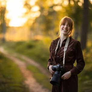 Portret van een vrouw in het bos die een leren camera strap draagt van The Hantler