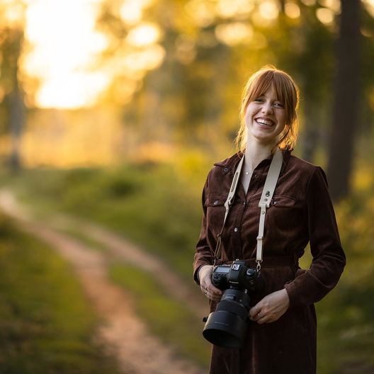 Portret van een vrouw in het bos die een leren camera strap draagt van The Hantler